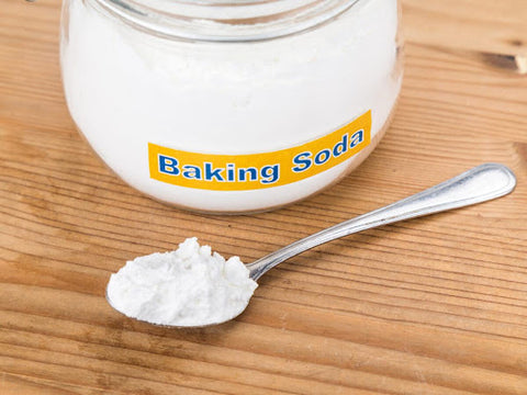 A spoon with baking soda sitting in front of a glass jar of baking soda