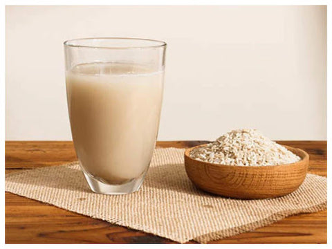 A glass of rice water and a wooden bowl full of rice sitting on a woven cloth