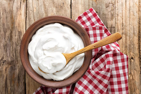 A bowl of plain yoghurt in a bowl with a wooden spoon inside the bowl that is sitting on a red and white cloth