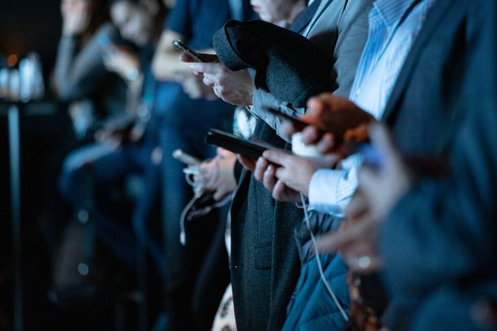 people lined up on phones, dark background, blue shirt, dark gray jacket, sports bar